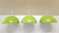 Front view of three lime green dome-shaped pendant light shades hanging side by side.