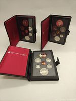 Three Royal Canadian Mint coin sets displayed in black presentation cases with red inner lining, showing multiple coins including large double dollar coins.