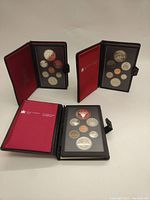 Three open coin sets displayed on a surface showing front view of coin holders and cases.