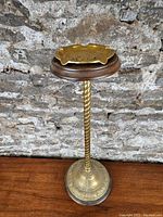Full view of ashtray mounted on tall wood and brass stand against brick backdrop