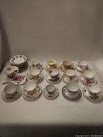 Photo showing front full view of all tea cup and plate sets arranged in rows on white background.