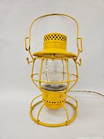 Front view of yellow CNR railway lantern converted to lamp, showing protective wire cage and clear glass globe with 'CNR' marking.