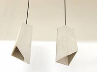 Two concrete geometric pendant light shades hanging from black wires against a white ceiling.