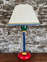 Full view of the Memphis style table lamp showing cream shade with colorful trim and vibrant base with red, blue, yellow, and green
