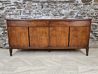 Front view of walnut credenza showing two top drawers and four cabinet doors against a stone wall.