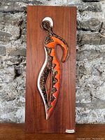 Front view of ceramic figure mounted on teak panel against stone background showing overall design and colors