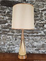 Front view of the entire lamp showing the tall cylindrical off-white fabric shade and decorated ceramic and wood base