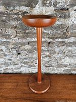 Front view of mid-century teak ashtray stand against textured stone wall background.
