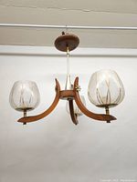 Full view of three-armed chandelier hanging from ceiling showing walnut arms, brass stem and three frosted glass globes