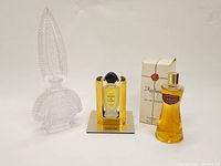 Three perfume bottles on white background: clear ornate bottle with stopper, Cartier Panthère parfum in gold-black case, Raphaël Réplique fragrance bottle with box.