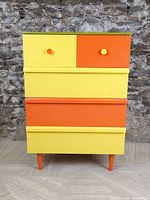 Front view of the painted dresser showing alternating yellow and orange drawer fronts with yellow and orange knobs.