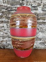 Full front view of the West German art pottery vase showing red glaze with textured horizontal bands in brown and ochre colors.