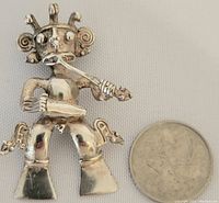 Photo of silver figural pendant shaped as a person playing violin with a coin for size reference.