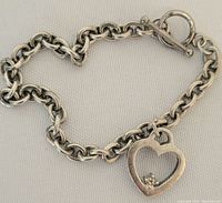 Full view of silver toggle bracelet with heart charm on light background