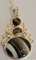 Front view of silver pendant with three banded agate stones and two clear stones set with decorative scrollwork.