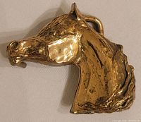 Front angled close-up view of brass horse head belt buckle, showing detailed mane and ear, smooth shiny surface with minor natural wear.