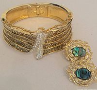 Full view of the gold tone clamper bracelet and matching earrings showing the rhinestone accent on bracelet and abalone shell inlay on earrings.