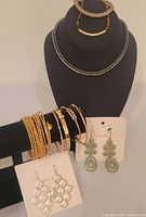 Full view of jewelry lot on display includes choker necklace, rope bracelets on stand, four gold-tone bangles and snake bracelet on bracelet display, two pairs of dangle earrings on cards.