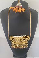 Full view of necklace displayed on bust, showing long braided cord and large decorated panel.