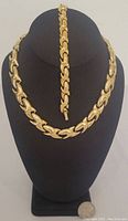 Overall view of matching gold tone necklace and bracelet set displayed on black stand.