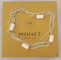 Photo of the Monet necklace coiled on top of the original box with brand and logo visible.
