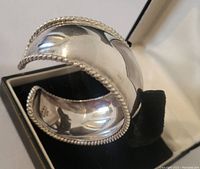 Close-up of polished sterling silver cuff with twisted rope edges showing reflective surface and adjustable opening.