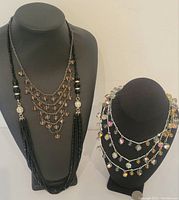 Photo showing two black and one brown/tan glass bead necklaces displayed on black necklace busts.