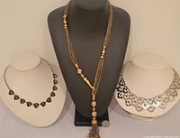 All three Stella & Dot necklaces shown on display busts: silver bib necklace, faceted glass dark gray necklace, and long gold-tone chain necklace with beads and tassel.