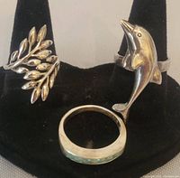 Three sterling silver rings displayed on a black stand, showing overall condition and design - leaf, dolphin, and turquoise stone band