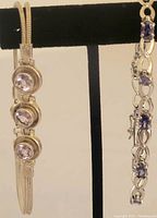 Two silver bracelets displayed side by side on black stand, showing different stone settings and bracelet styles.