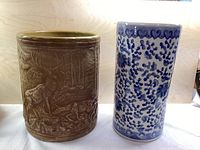 Photo showing both umbrella stands side by side: the brown ceramic with elk relief and the blue floral porcelain
