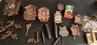Image showing full collection of cuckoo clocks and parts, including wooden carved clocks, cat-shaped decorative clocks, pinecone weights, and a boxed clock.