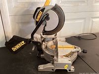 Left side view of saw on black surface showing blade, guard, handle and dust bag attached