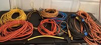 Several coiled extension cords in multiple colors laid out on table, showing quantity and condition.
