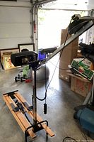 Side view showing the wooden base frame, foot pedals with straps, and the vertical support arm with monitor and control buttons.