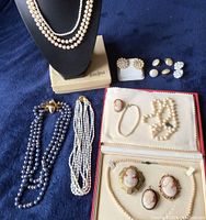 All items laid out on dark blue cloth: six necklaces on bust and table, bracelet, cameos, earrings