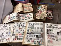 Four open albums/stockbooks on table and a box of loose stamps with a collector’s guide booklet