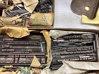 Multiple boxes containing vintage metal letterpress letters, some neatly organized with visible reversed text, others in loose piles with paper wrapping.