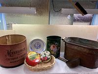 Overview of lot showing large wooden cheese bin, decorative tins, woven basket, plated, copper pot and ladle