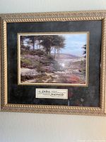 Framed artwork with gold ornate frame and black mat, landscape of sheep and countryside, label with artist name visible