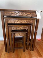 Stacked set of 4 wooden nesting tables with carved details on front sides of each table.