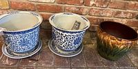 Wide view of three ceramic pots including two white and blue floral pattern pots with saucers and one brown and green glazed pot.