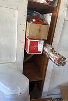 Wooden shelf with cardboard boxes containing Christmas decorations and gift wrap rolls leaning on the side