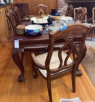 Dining table surrounded by six chairs, showing wood and cushioned seats, various small items on the table surface.