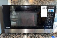 Front view of Panasonic microwave showing large glass door, stainless steel trim, and control panel with digital display and buttons.