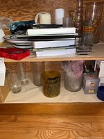 Glass vases of different colors and sizes, stacked dishes, and assorted items on two wooden shelves