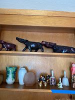 Top shelf with black carved wooden animal sculptures including crocodile, wolf, and another animal; bottom shelf with small ceramic vases and figurines