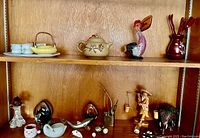Two wooden shelves in a cabinet with ceramic and wooden sculptures, along with Asian tea sets and various decorative items.