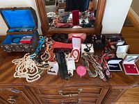 Top view of dresser with multiple pieces of jewelry including bracelets, necklaces, rings, sunglasses, and jewelry boxes.