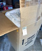 White queen size mattress topper partially folded inside large cardboard box with 'Fragile' and handling instructions visible.